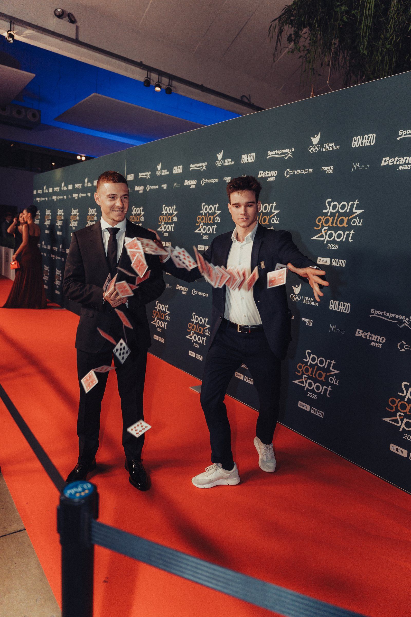 Jonas De Bruyn performing card magic on the red carpet at a sports gala, sponsor wall behind