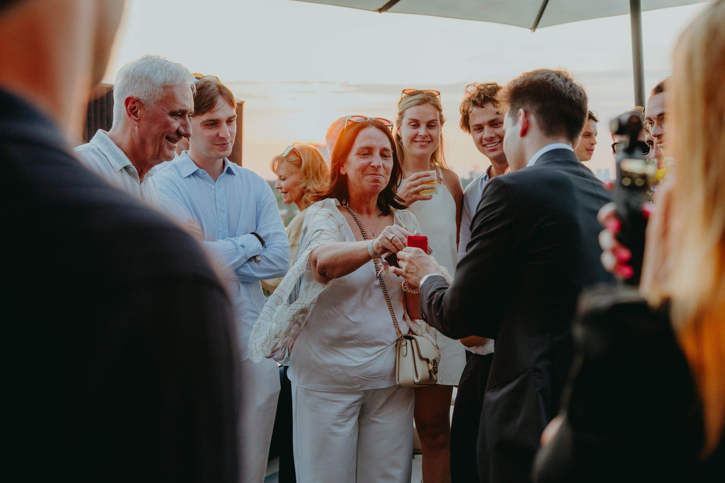 Jonas De Bruyn performing an intimate card trick for delighted guests at a rooftop gathering, golden hour