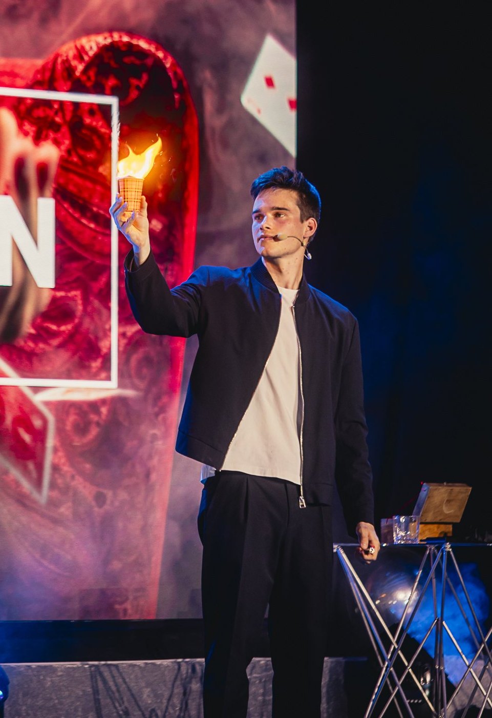 Jonas De Bruyn on stage holding a lit flame, his own branding lit up behind him