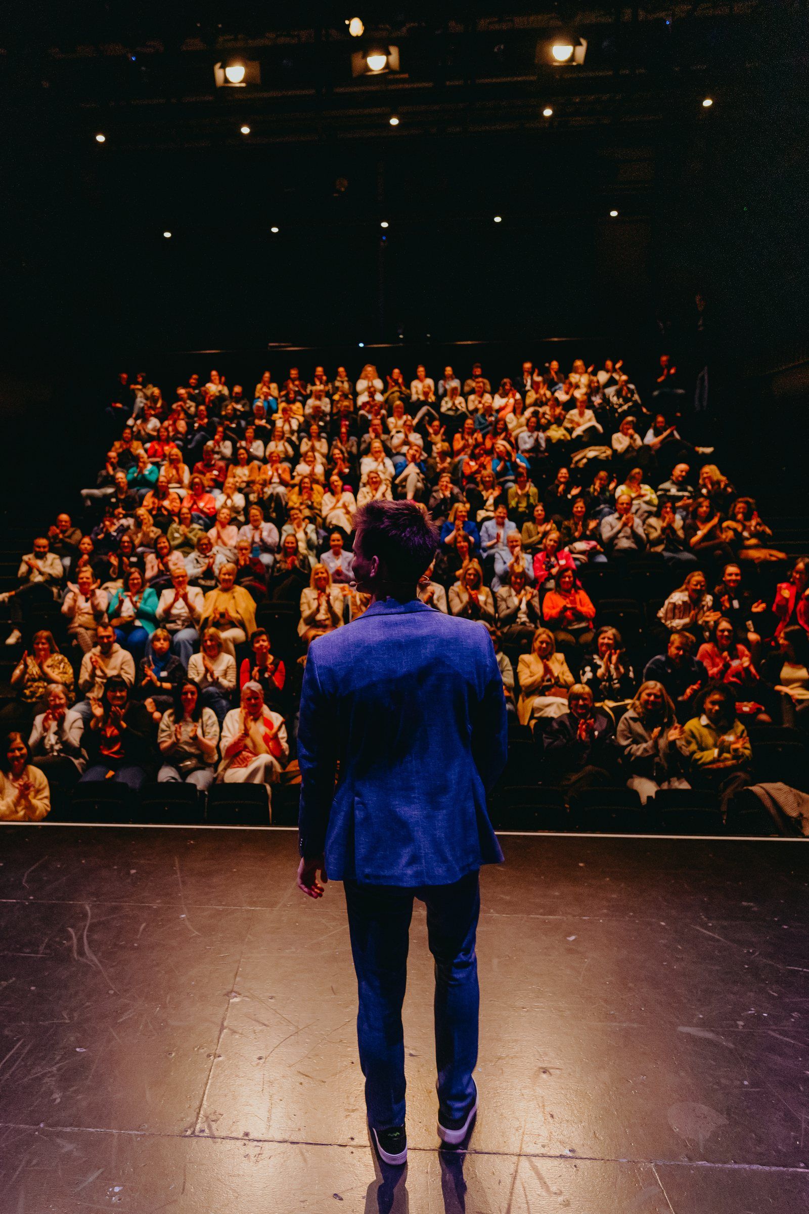 Jonas De Bruyn facing a full theatre audience applauding during a team event
